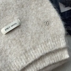 Detailed macro view of cream knitted wool scarf featuring ERET label and metal B charm