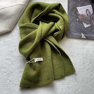 Detail of 100% wool moss green scarf with wash label on a soft stylish background