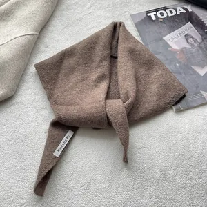 Détail d'une écharpe triangulaire en tricot marron avec étiquette sur un manteau de laine