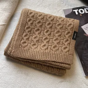 Detail showing thick cable-knit texture and 100% wool label of the brown winter scarf