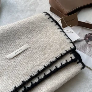 Dettaglio sciarpa in maglia crema con cucitura a contrasto nera ed etichetta BOWLOW
