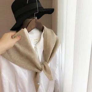 Détail du châle en tricot beige avec texture douce et étiquette sur chemise blanche