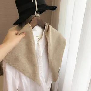 Détail de la texture du châle triangulaire en tricot beige sur chemise blanche