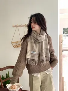 Detail of soft beige plaid wool scarf with fringe styled over a brown knit sweater