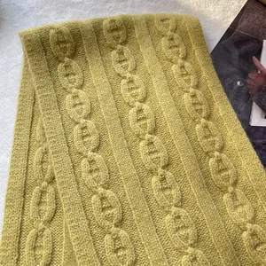 Detailed close-up of thick mustard green wool scarf with cable knit anchor chain patterns