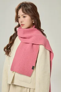 Detail eines rosa gestrickten Wollschals mit Rippenstruktur und schwarzem Etikett am Modell