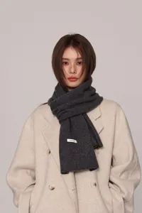 Detailed view of dark grey 100% pure wool scarf with woven label on a beige coat
