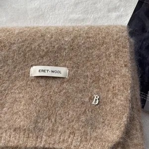 Macro detail of camel wool scarf featuring branded woven label and silver B-letter charm