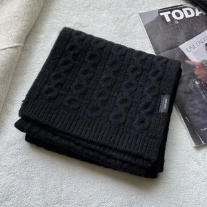Detailed view of black cable-knit wool scarf with 100% wool label on textured fabric
