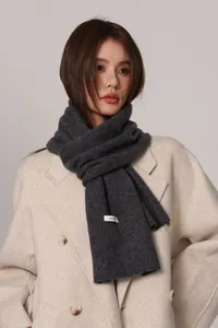 Close-up of 100% pure wool scarf tag showing premium knit texture on gray winter shawl