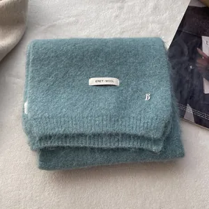 Detailed view of teal knit wool scarf featuring brand label and silver metal B logo charm