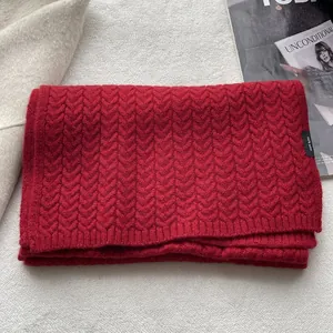 Dettaglio di una sciarpa rossa in 100% lana con trama a trecce ed etichetta di lavaggio