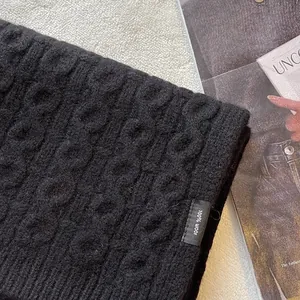 Close-up of 100% wool knit scarf featuring a classic cable pattern and quality tag