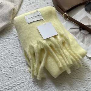 Close-up of soft yellow cashmere-like scarf with fringe detail and minimalist brand label