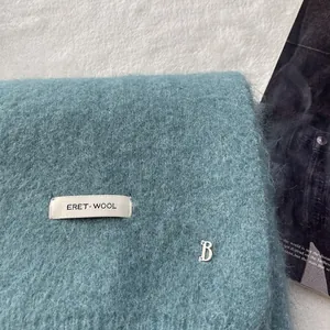 Close-up of teal wool knit scarf showing long hair texture and silver metal B logo charm
