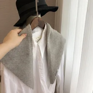 Détail d'un châle triangulaire en tricot gris clair drapé sur une chemise blanche