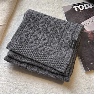 Detail view of high-quality 100% grey wool scarf with classic cable knit texture and tag