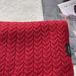 Dettaglio di sciarpa rossa 100% lana con trama a maglia spessa e etichetta materiale