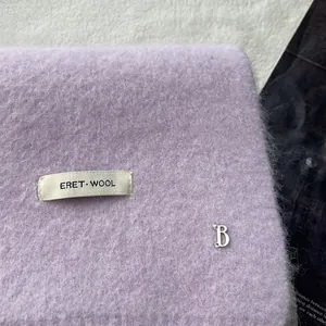 Macro shot of soft lavender wool knit scarf featuring metal B charm and woven brand label