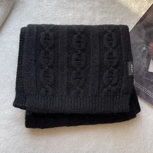 Detail showing the 100% wool label and chain-knit texture on a black scarf