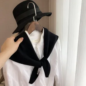 Détail d'un châle triangulaire en tricot noir noué sur une chemise blanche avec étiquette