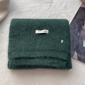 Detailed macro view of dark green knit wool scarf with ERET WOOL label and metal B logo