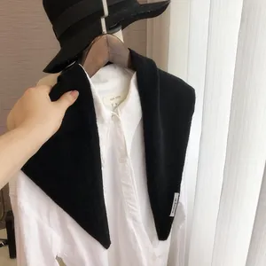 Détail d'un châle en laine tricotée noire sur une chemise blanche sur un cintre en bois