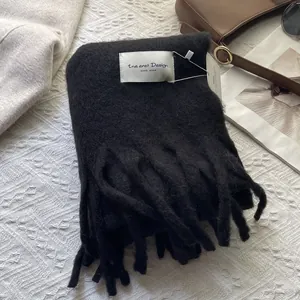 Detail of black wool scarf with long tassels and handmade label on soft knit fabric
