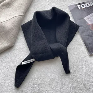 Gros plan d'une écharpe en maille noire avec étiquette sur fond gris minimaliste