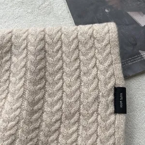 Dettaglio ravvicinato della sciarpa in maglia a trecce 100% pura lana beige e etichetta