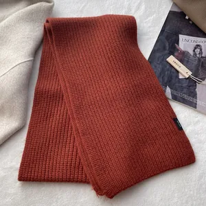 Detail eines 100% Wollschals in Dunkelorange mit grober Strickstruktur auf weißem Filz