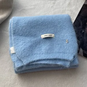 Detail of light blue wool knit scarf with brand label and golden B metal ornament