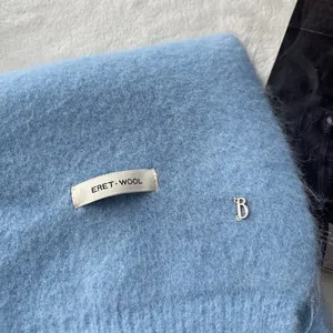 Detailed texture of light blue wool scarf with silver letter B charm and woven label