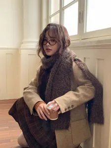 Detail of a warm creamy yellow woolen scarf styled with a khaki coat and plaid skirt