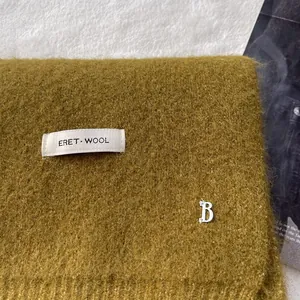 Macro view of ginger wool scarf featuring a silver letter B pendant and woven label