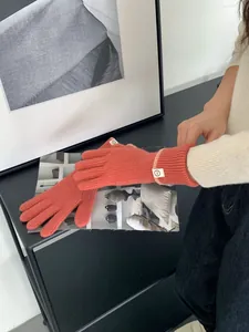 Détail de gants en maille orange corail avec poignets côtelés et petite étiquette en tissu