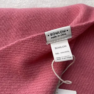 Detailed macro shot of the 100% pure wool texture and official brand label on pink scarf