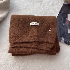 Detailed close-up of dark brown knitted wool scarf featuring a woven label and metal B charm