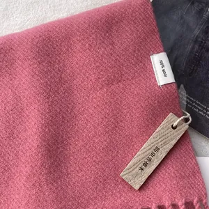 Detail of pink wool scarf with fringe, 100% wool label and cedar wood anti-moth tag