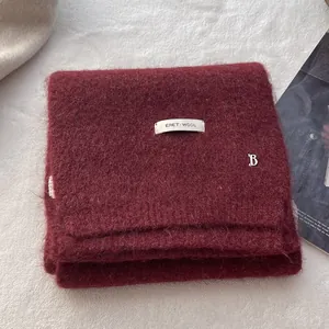 Close-up of wine red wool knit scarf with soft brushed texture and metal B pendant