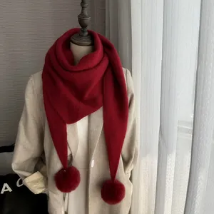 Détail de la maille d'une écharpe triangle rouge foncé avec pompons en fausse fourrure