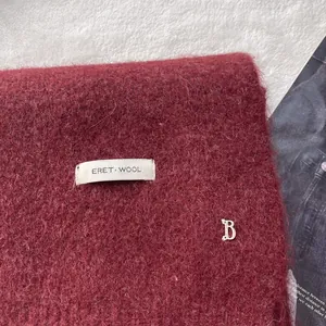 Detail of burgundy wool knit scarf featuring a white ERET WOOL label and silver B charm
