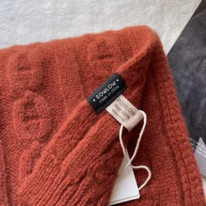 Close-up of 100% pure wool orange cable knit scarf with brand label and fine texture