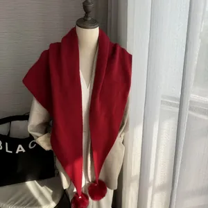 Détail d'une écharpe triangle tricotée bordeaux avec pompons en fausse fourrure douce