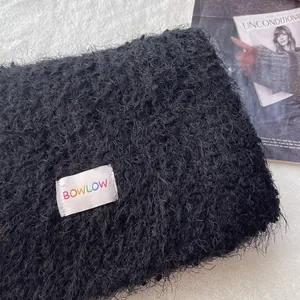 Detail view of black plush wool scarf with white BOWLOW woven label and soft texture