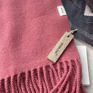 Close-up of pink 100% wool scarf texture with soft fringe and premium brand tag