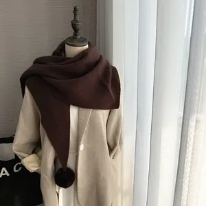 Détail d'une écharpe en maille marron foncé avec pompon en fausse fourrure sur manteau