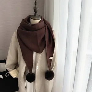 Détail de l'écharpe en maille marron foncé avec pompons en fausse fourrure et texture douce