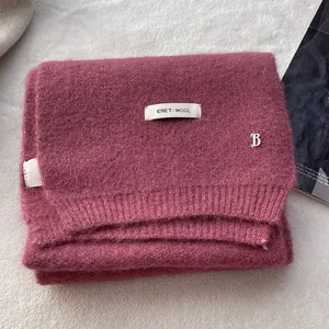 Detailed macro view of plum pink wool knit scarf with silver B pendant and fabric label