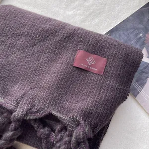 Détail d'écharpe à carreaux violet et gris avec de grosses franges tressées et logo